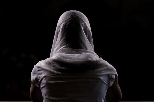 Silhouette of a young girl who sits in church and praying. Close-up view from behind. Backlight.