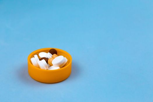 Dose of the colored pills in the cap of the package of pills. On blue background with copy space for text.