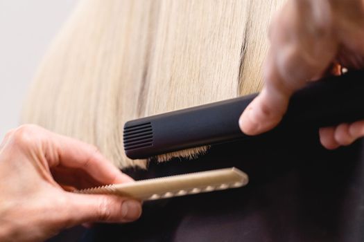 Hairdresser using a flat iron hair straightener to straighten woman's blonde hair