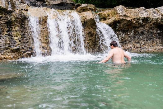 Tropical nature and vacation. Man swimming in the mountain river with a waterfall