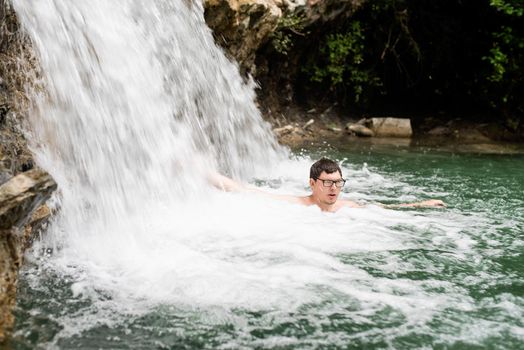 Tropical nature and vacation. Man swimming in the mountain river with a waterfall