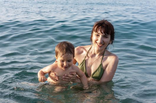 Happy family and healthy lifestyle. Young mom teaches a child to swim in the sea
