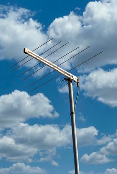 A metal television antenna on a a house roof against a blue sky background