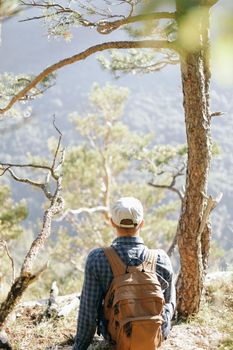 Backpacker young man resting near the tree and enjoying view of nature.