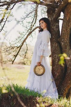 Portrait of carefree young woman in white vintage wedding style dress in spring cherry blossom garden valley.