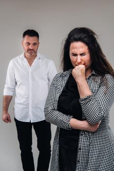 A woman beaten by her husband standing behind her and looking at her aggressively. Domestic violence.