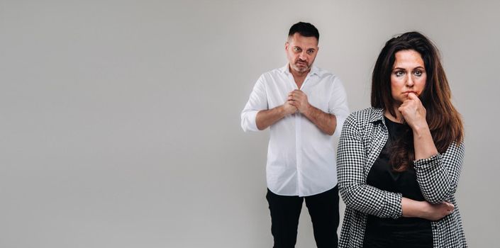 A woman beaten by a man stands on a gray background. Domestic violence.