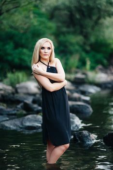 blonde girl in a black dress with blue eyes on the stone coast of the river