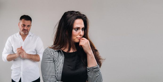 A woman beaten by a man stands on a gray background. Domestic violence.