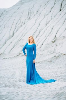 blonde girl in a blue dress with blue eyes in a granite quarry against the background of gravel