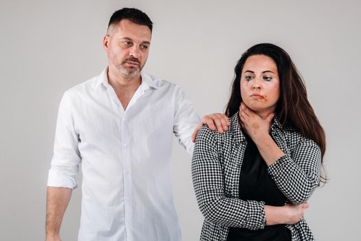 A woman beaten by her husband standing behind her and looking at her aggressively. Domestic violence.