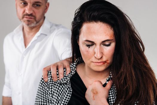 A woman beaten by her husband standing behind her and looking at her aggressively. Domestic violence.