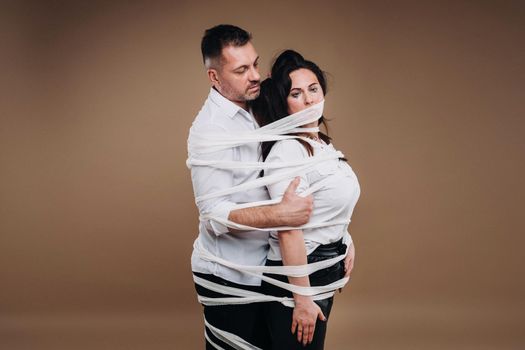 An aggressive man embraces a battered woman and is wrapped in bandages together. Domestic violence.