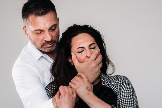 An aggressive man covers the mouth of a beaten woman so that she cannot scream. Domestic violence.