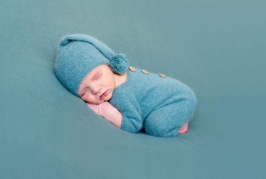 Infant baby boy sleeping in woolen costume with bare feet on blue blanket. Dreamy little child sleeps