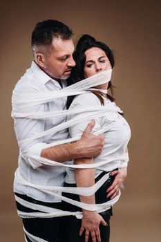 An aggressive man embraces a battered woman and is wrapped in bandages together. Domestic violence.