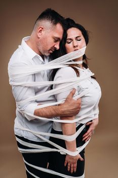 An aggressive man embraces a battered woman and is wrapped in bandages together. Domestic violence.