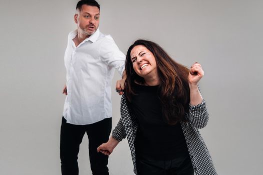 A man swings his fist at a battered woman standing on a gray background. Domestic violence.