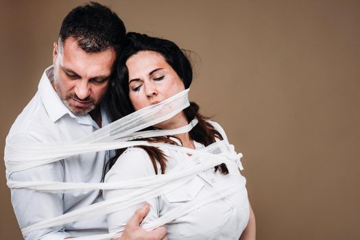 An aggressive man embraces a battered woman and is wrapped in bandages together. Domestic violence.