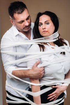 An aggressive man embraces a battered woman and is wrapped in bandages together. Domestic violence.