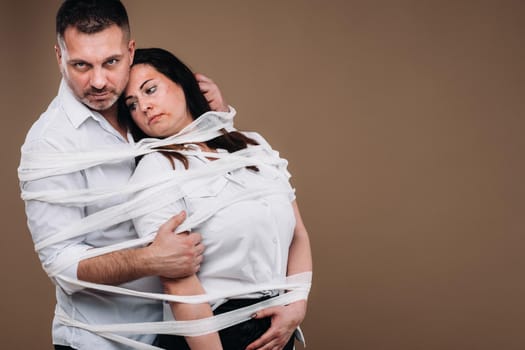 An aggressive man embraces a battered woman and is wrapped in bandages together. Domestic violence.