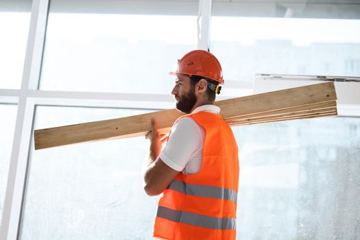 Builder man in hardhat carrying timber on building site, close up portrait