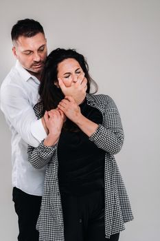 An aggressive man covers the mouth of a beaten woman so that she cannot scream. Domestic violence.