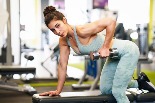 Caucasian strong woman lifting some weights and working on her triceps and biceps in a gym with dumbbells.