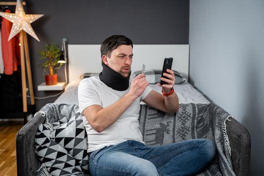 Man after accident in cervical collar consults online video call with doctor and receives recommendations for taking medications. Male in foam cervical spinal injury video conferencing with insurance.