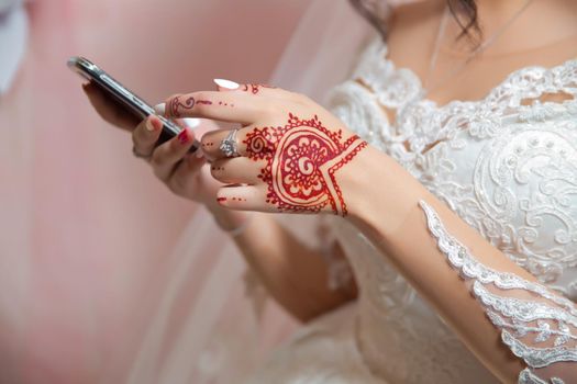 The bride holds a phone . The bride has a ring in her hands . The bride has a henna.