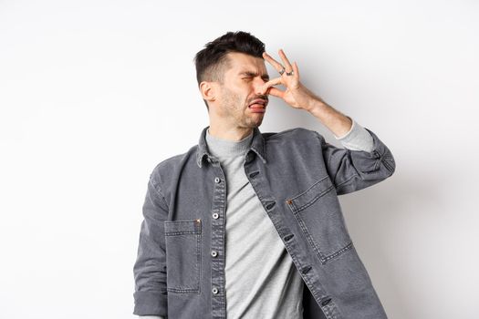 Disgusted man turn away and shut nose from bad smell, disgusting reek, standing on white background.