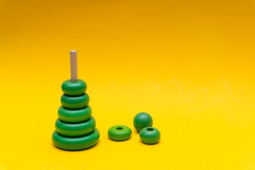 Pyramid build from green children wooden toy rings at yellow background, toy for baby and toddlers. Child development concept.