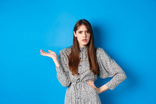 Confused and annoyed girl arguing, raising hand up and frowning, cant understand what big deal, standing on blue background.