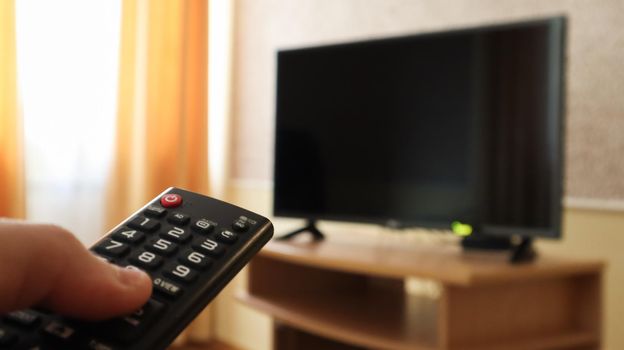 Hand holding a television remote control and surfing programs on television. watch, turn on or off the TV in the living room or bedroom on the black-screen nightstand. Copy space