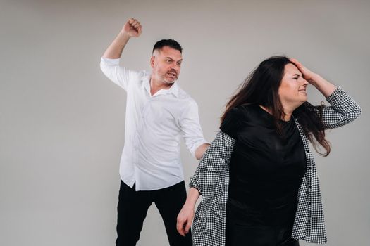 A man swings his hand at a battered woman standing on a gray background. Domestic violence.