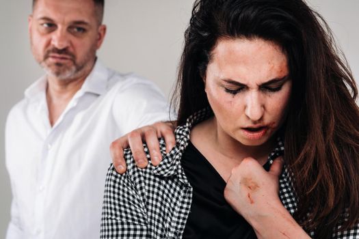 A woman beaten by her husband standing behind her and looking at her aggressively. Domestic violence.