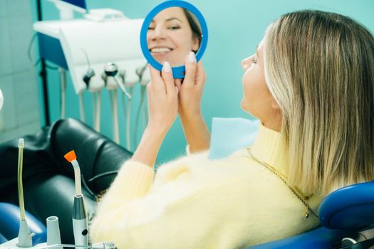 The girl smiles and looks in the mirror in dentistry.