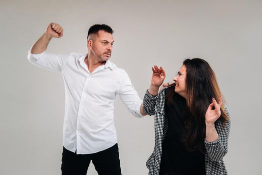 A man swings his fist at a battered woman standing on a gray background. Domestic violence.