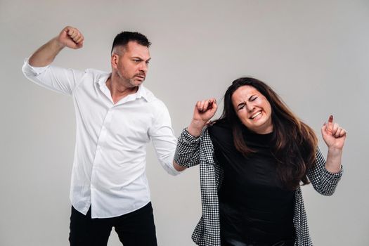 A man swings his fist at a battered woman standing on a gray background. Domestic violence.