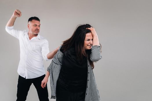 A man swings his fist at a battered woman standing on a gray background. Domestic violence.