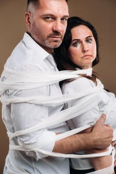 An aggressive man embraces a battered woman and is wrapped in bandages together. Domestic violence.