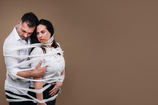 An aggressive man embraces a battered woman and is wrapped in bandages together. Domestic violence.