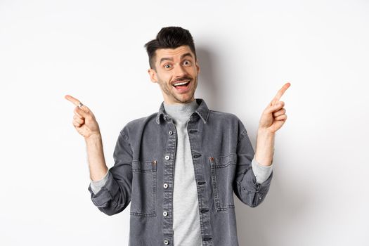 Cheerful smiling man pointing fingers sideways, showing left and right ways, looking happy at camera, standing on white background.