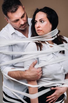 An aggressive man embraces a battered woman and is wrapped in bandages together. Domestic violence.