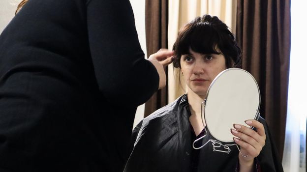 Close up of master hairdresser doing curly hairstyle and makeup for beautiful woman with dark hair at home. Wedding hairstyle for the bride