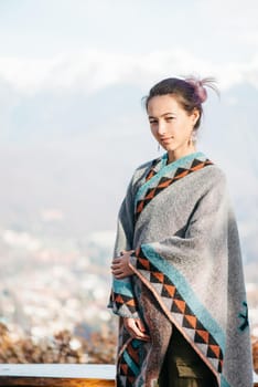 Beautiful young woman standing on background of snowy mountains, looking at camera.