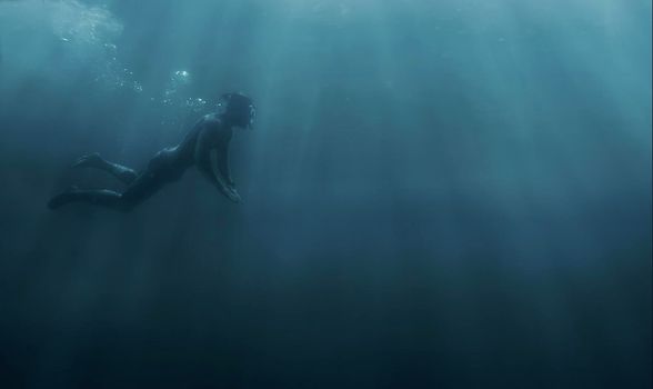 Male freediver swimming with mask and snorkel underwater in deep sea, copy-space in the right part of the image.