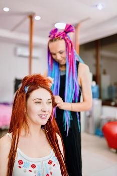 Barber braids dreadlocks. Hippie and boho style coiffure with kanekalon. Beauty salon services. Hairdresser weaves to funny redhead girl ginger afro pigtails.