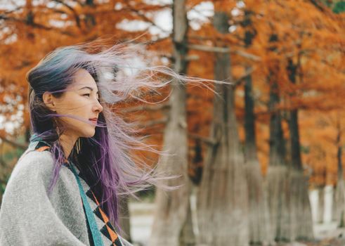 Beautiful young woman walking in windy weather in autumn park.