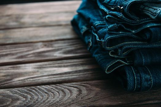 Stack of blue jeans denim pants on a wooden table.